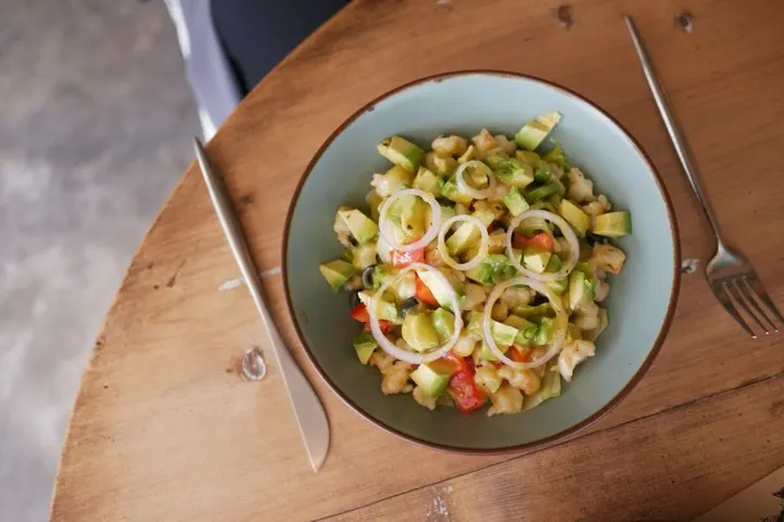 Salada fresca com abacate e legumes numa tigela, na mesa de madeira